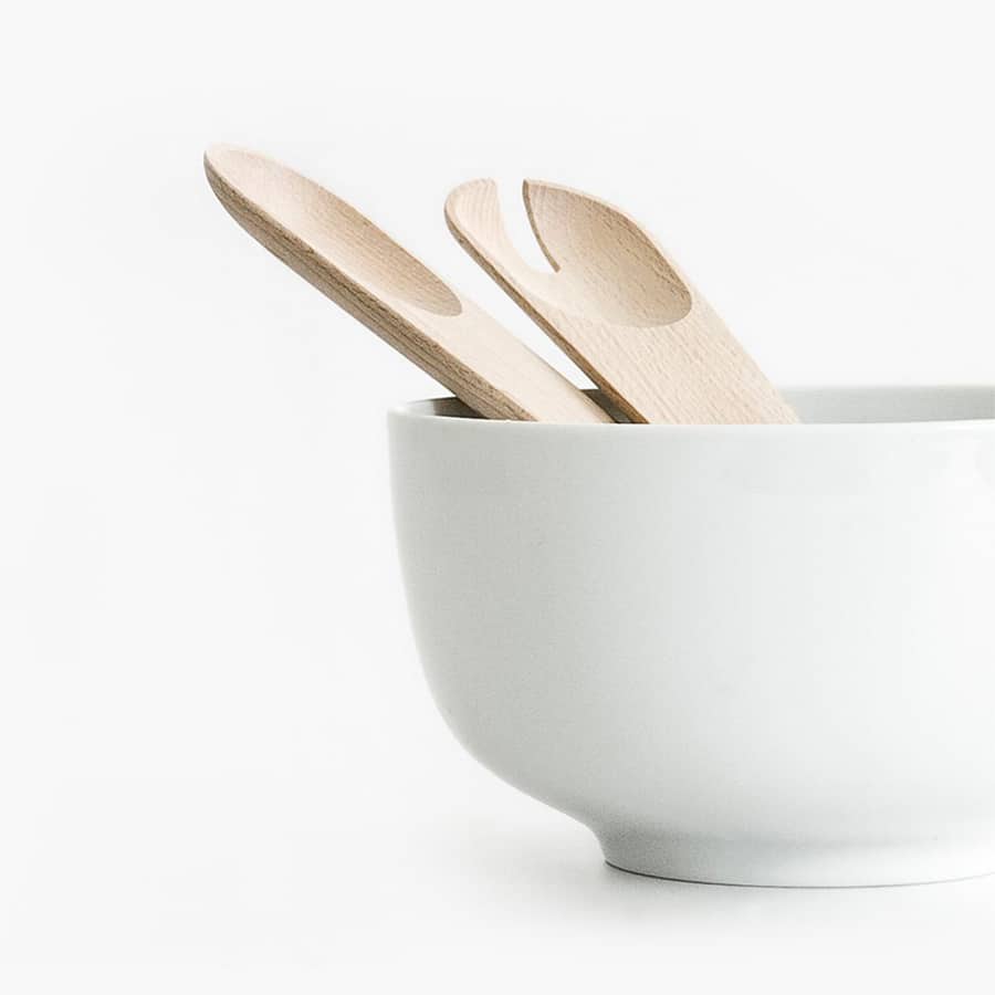 White bowl with wooden salad utensils.