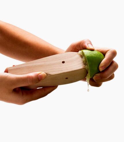 Hand squeezing lime with wooden citrus reamer.