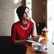 Woman in red sitting by window, reading.