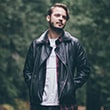 Man in leather jacket standing in forest.