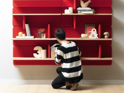 Person organizing items on red wall shelves.