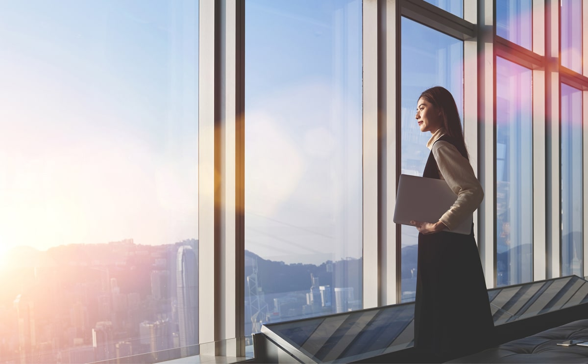 Woman holding laptop, looking out window.